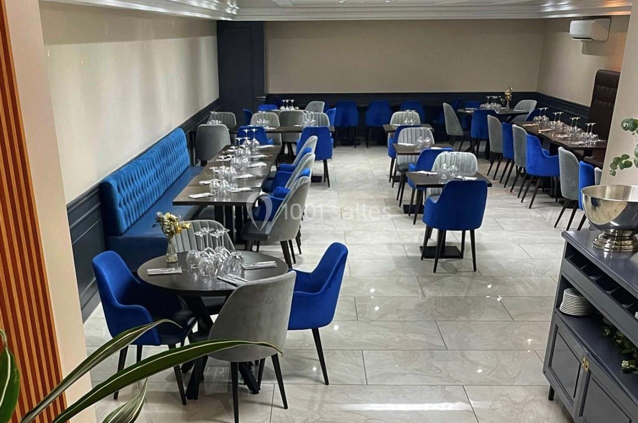 Salle de restaurant moderne avec tables dressées, chaises bleues et grises, et sol en carrelage clair.