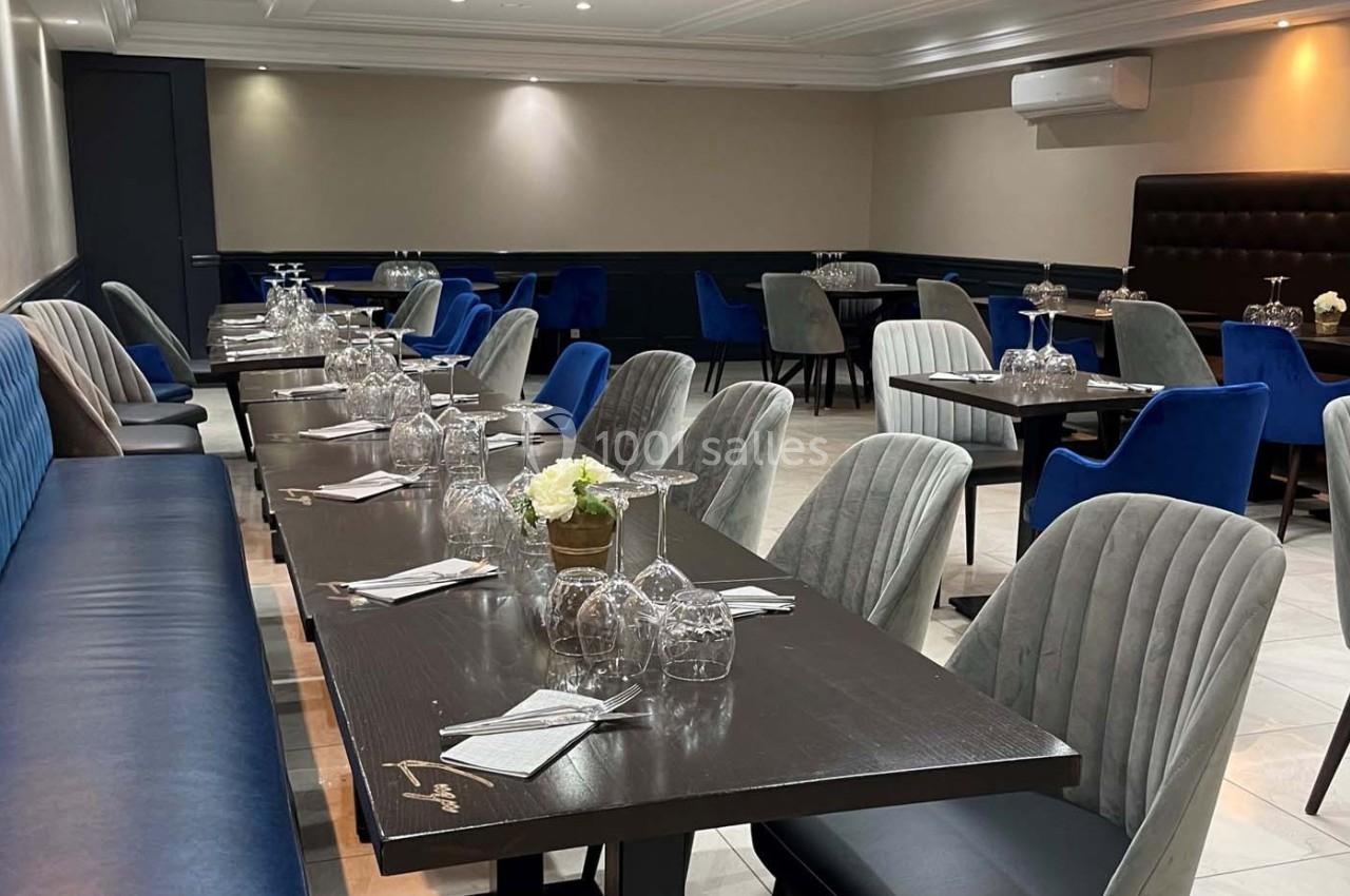 Salle de restaurant moderne avec tables dressées, chaises rembourrées grises et bleues, éclairage doux.