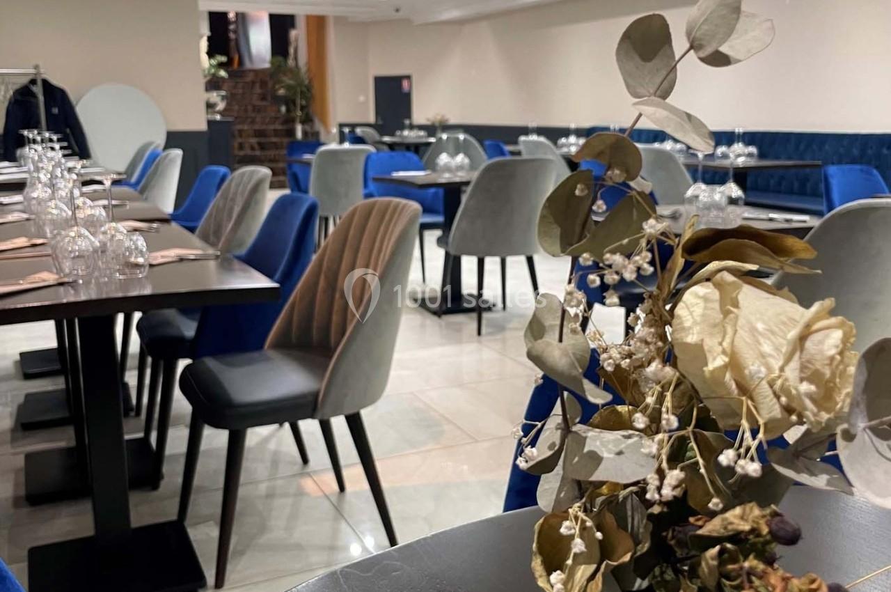 Salle de restaurant moderne avec tables dressées, chaises rembourrées bleues et grises, et décoration florale en premier…