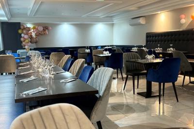 Salle de restaurant élégante avec tables dressées, chaises rembourrées et décoration florale en premier plan.