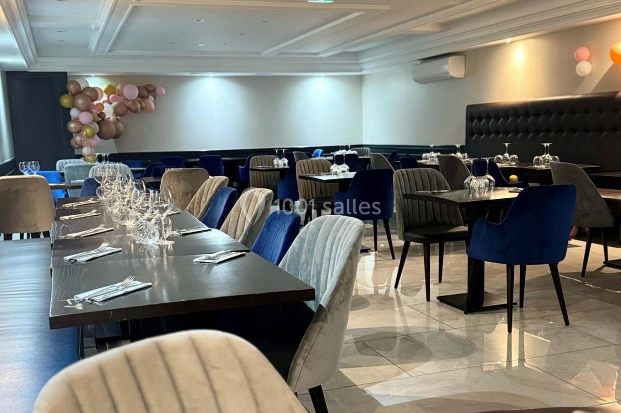 Salle de restaurant élégante avec tables dressées, chaises rembourrées et décorations de ballons en arrière-plan.