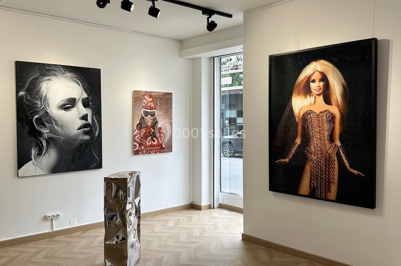 Vue d'une galerie d'art moderne avec des peintures accrochées aux murs et une sculpture métallique au centre.