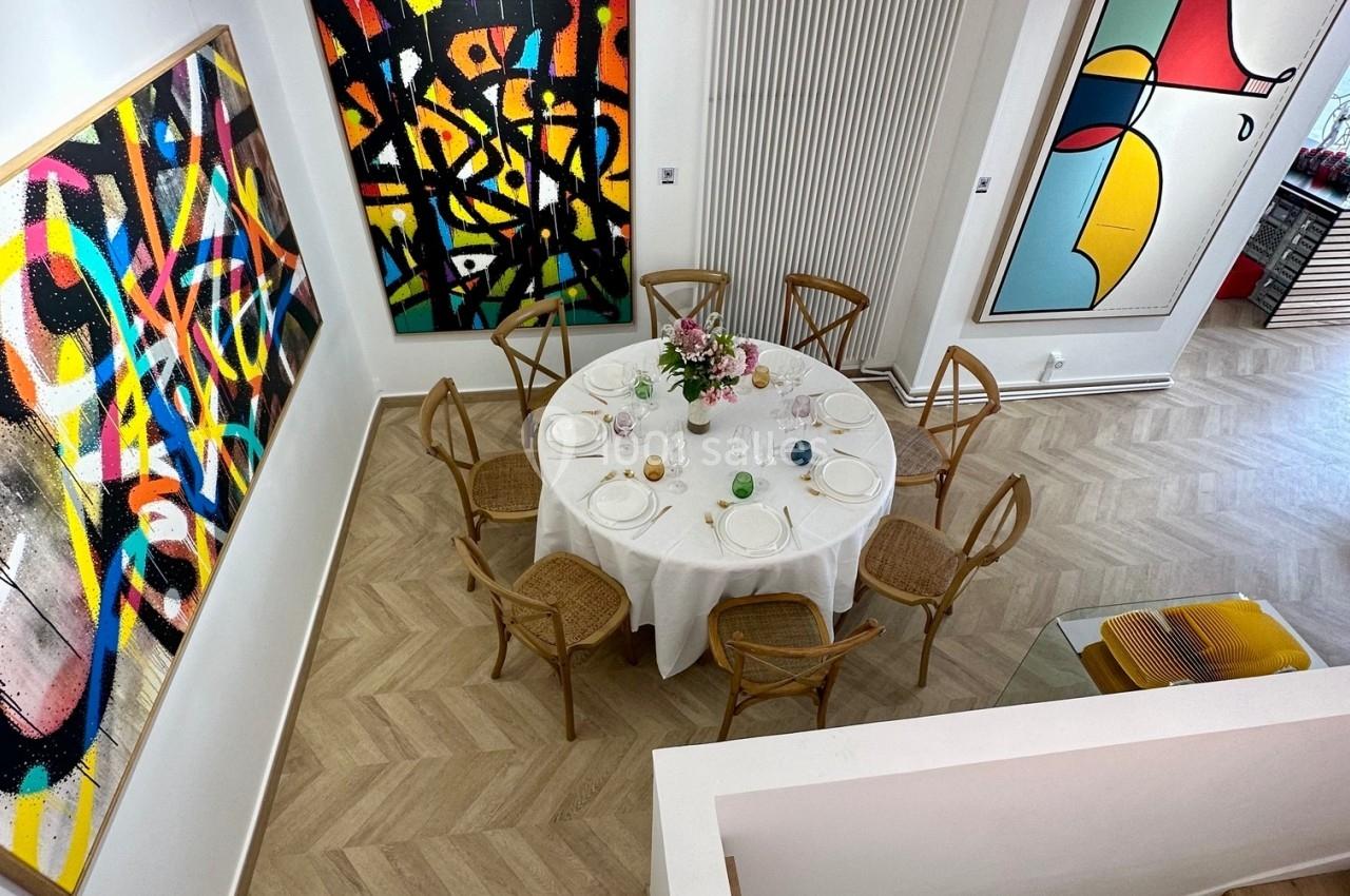 Vue d'une salle moderne avec une table ronde dressée, entourée de chaises en bois, et des tableaux abstraits accrochés aux…