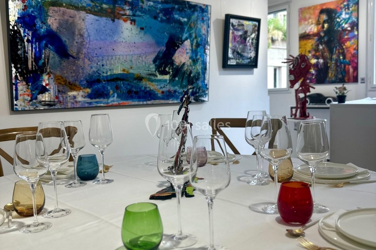 Table dressée avec vaisselle colorée dans une galerie d'art, entourée de peintures abstraites exposées sur les murs.