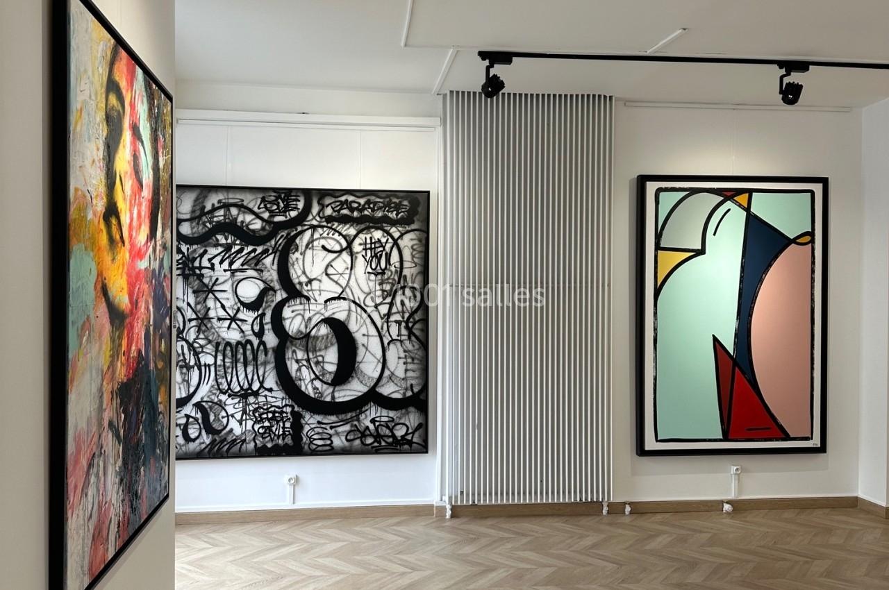 Salle d'exposition avec trois tableaux contemporains accrochés sur des murs blancs, éclairés par des spots.