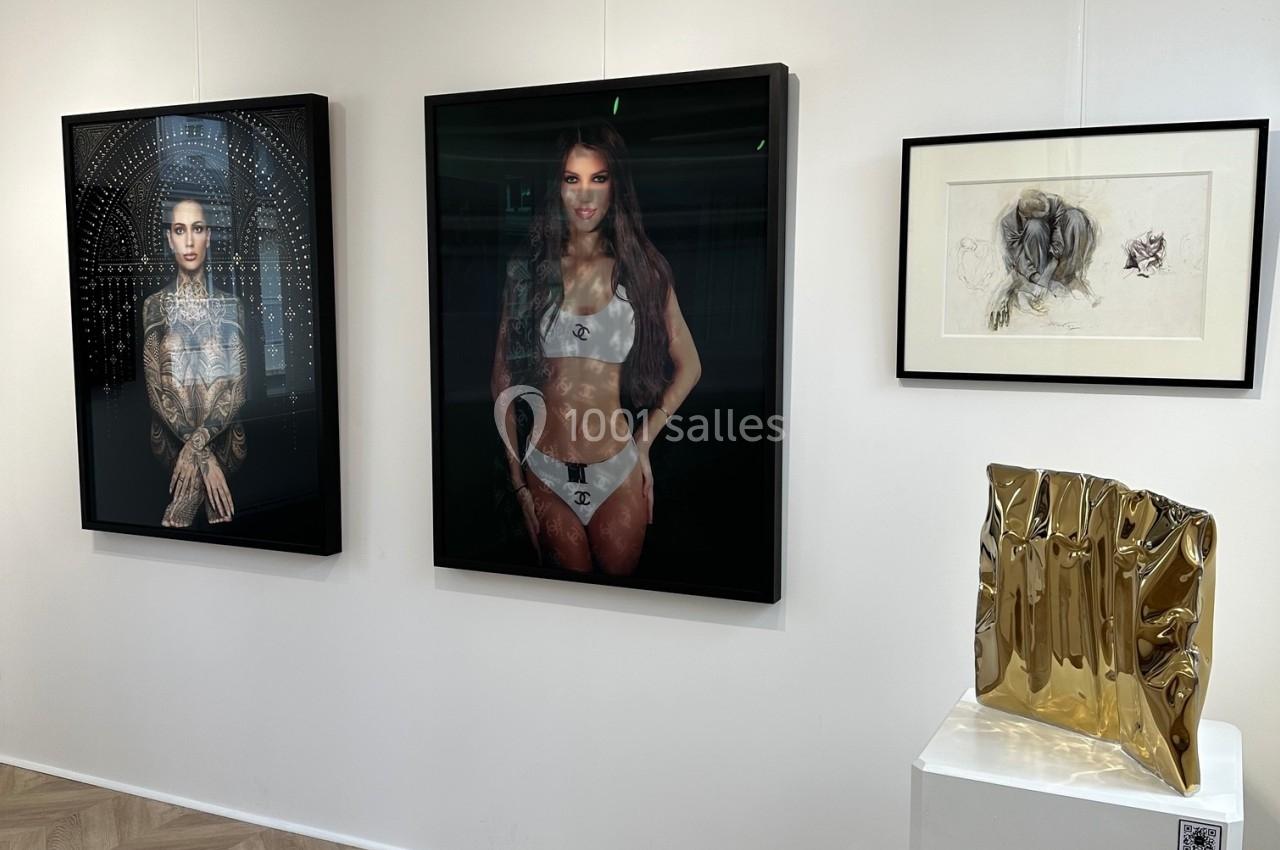 Vue d'une galerie d'art avec des photographies encadrées, un dessin et une sculpture dorée sur un socle.