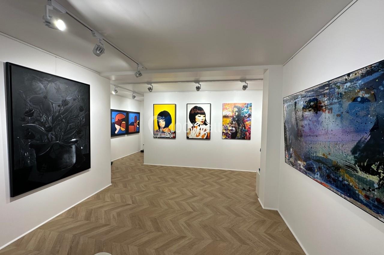 Vue d'une galerie d'art moderne avec des peintures colorées accrochées sur des murs blancs et un sol en parquet clair.