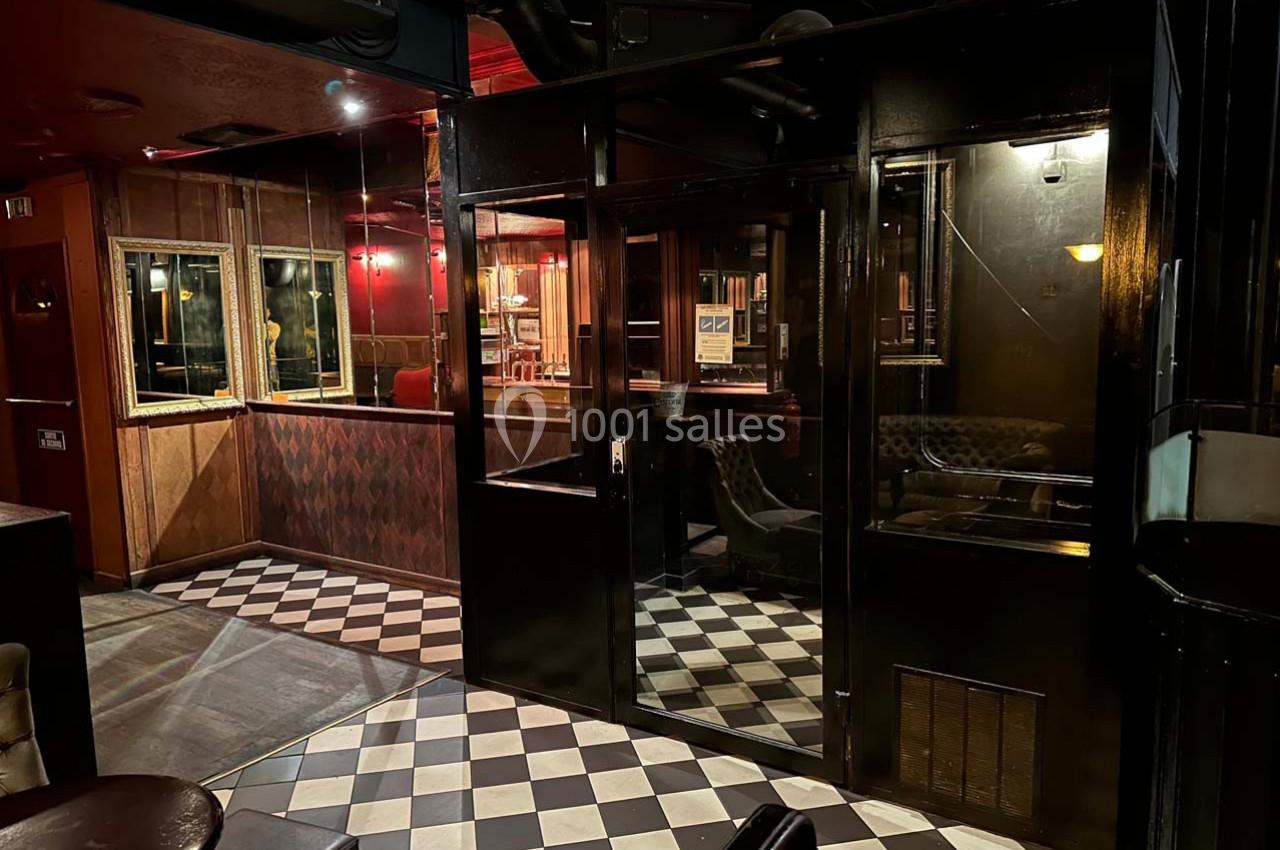 Intérieur d'un bar sombre avec des murs en bois, un sol à carreaux noir et blanc, et des sièges en cuir.