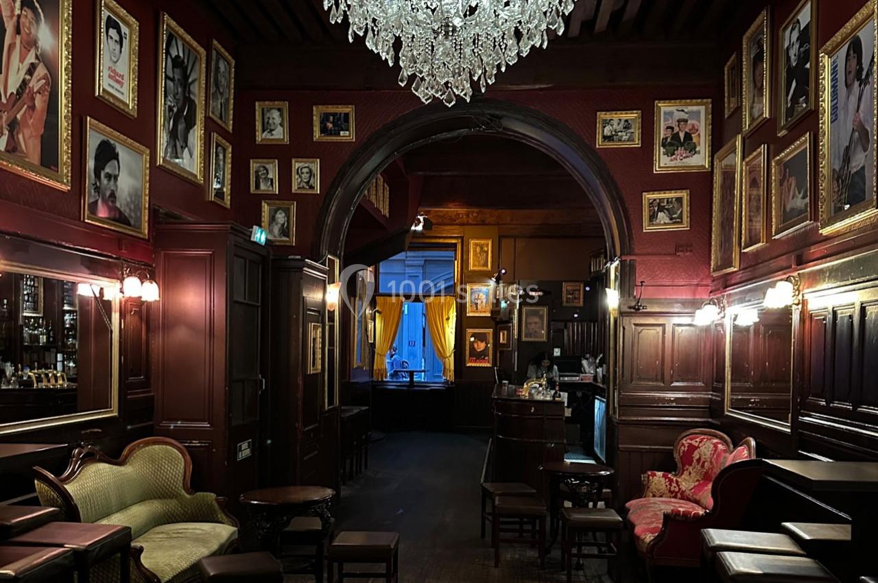 Intérieur d'un salon vintage avec murs ornés de portraits, lustre en cristal et mobilier ancien en bois et tissu.