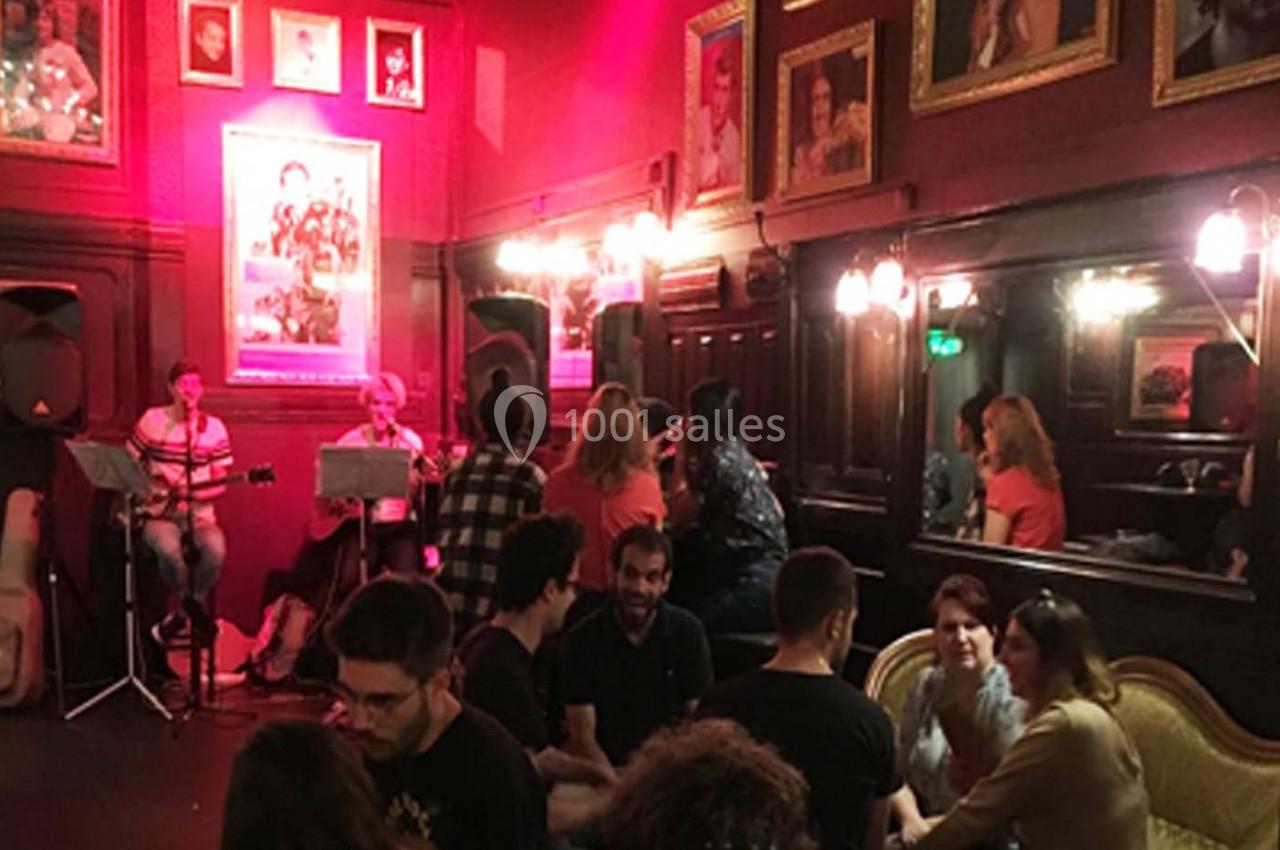 Des personnes discutent dans un bar à l'ambiance chaleureuse, avec des musiciens jouant en arrière-plan sous une lumière…
