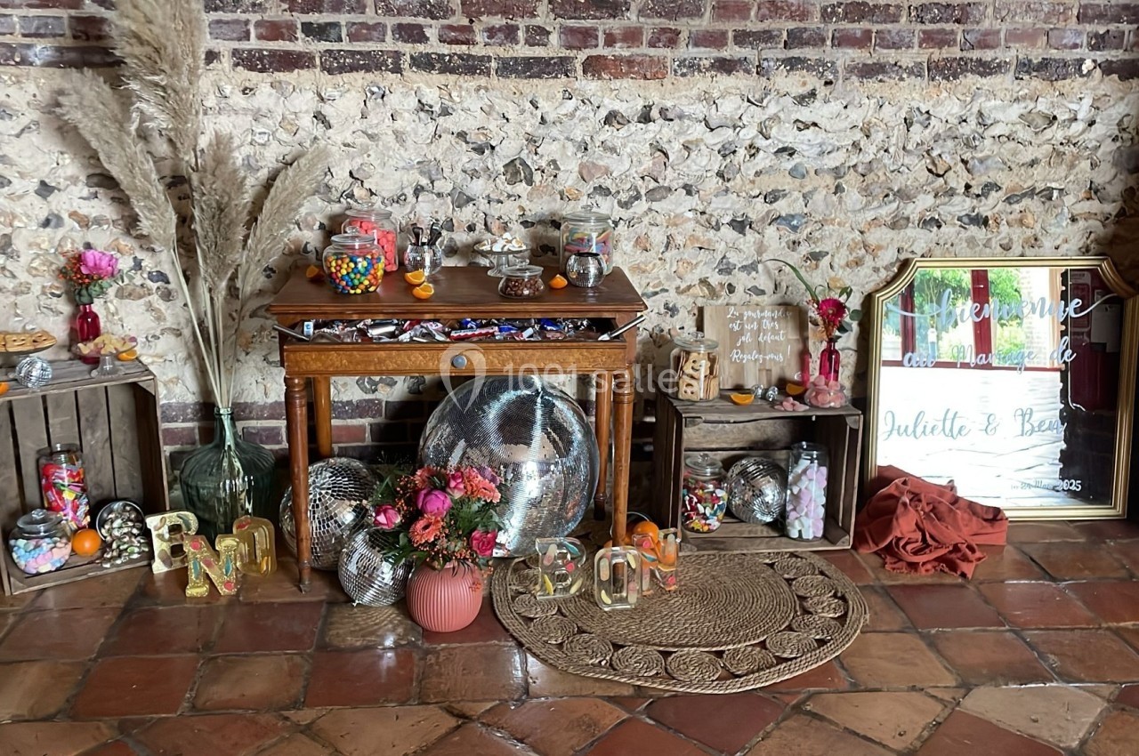Décoration de mariage avec table en bois, bonbonnières, fleurs, miroirs, et pancarte de bienvenue devant un mur en briques.