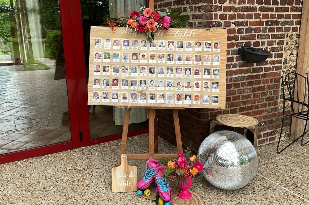 Tableau de plan de table décoré avec des fleurs colorées, posé sur un chevalet devant une porte vitrée.
