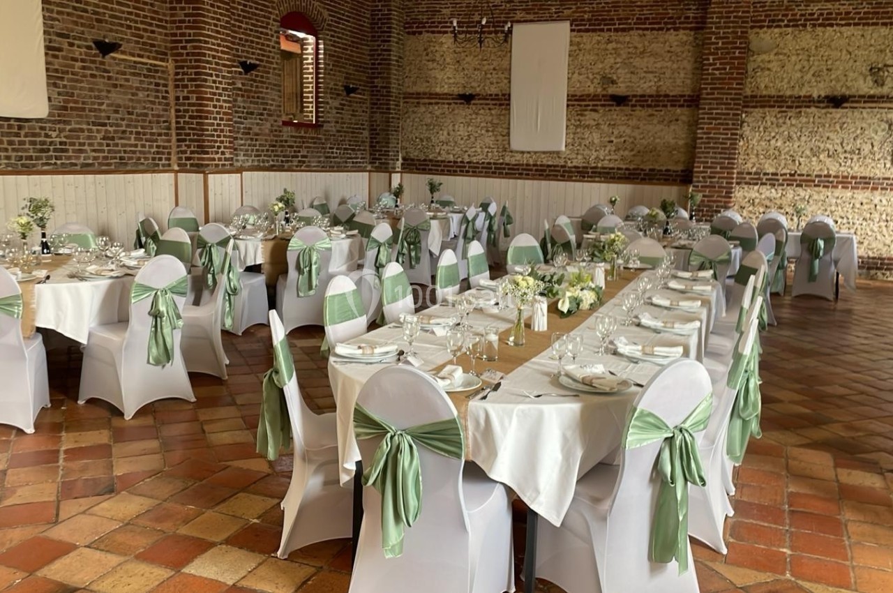 Salle de réception décorée avec des tables alignées, nappes blanches et chaises ornées de nœuds verts.