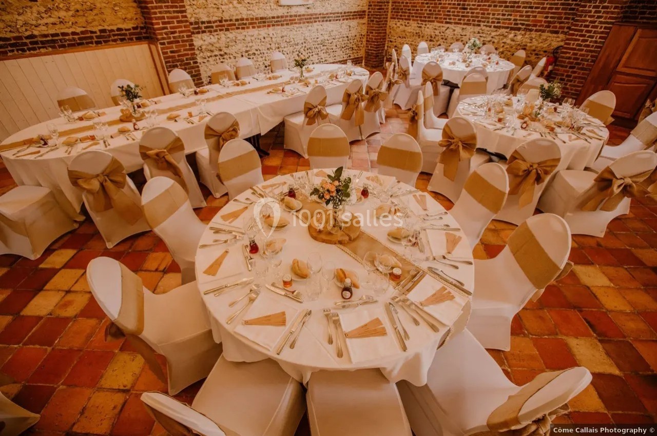 Salle de réception décorée avec des tables rondes et rectangulaires, nappes blanches et chaises ornées de nœuds beige.