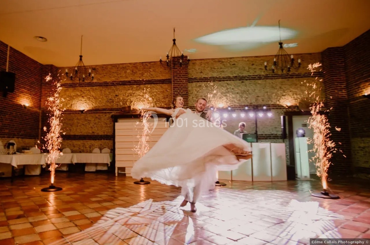 Un couple danse une valse dans une salle éclairée, entouré de gerbes d'étincelles et de murs en briques.