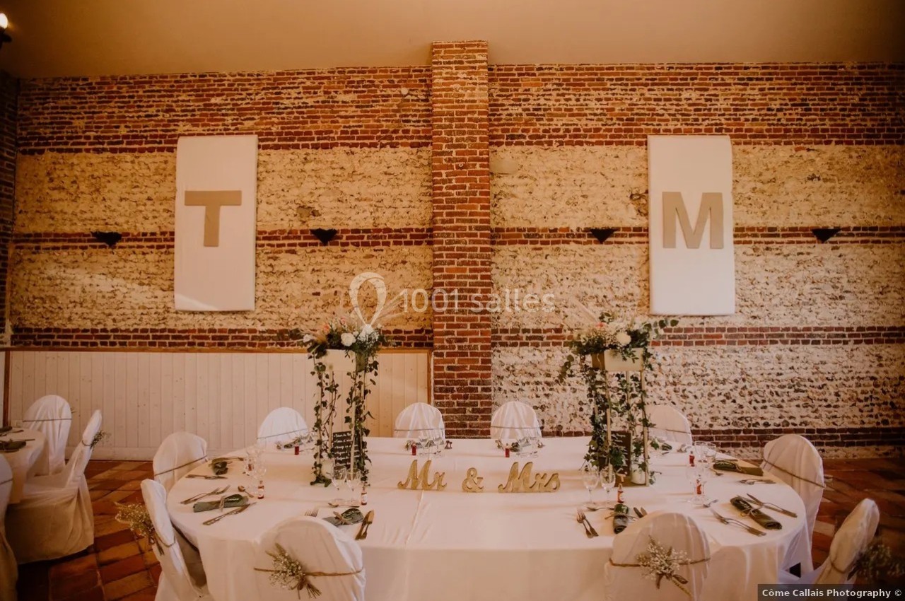 Salle de réception avec murs en briques, table décorée de fleurs et lettres ’T’ et ’M’ accrochées au mur.