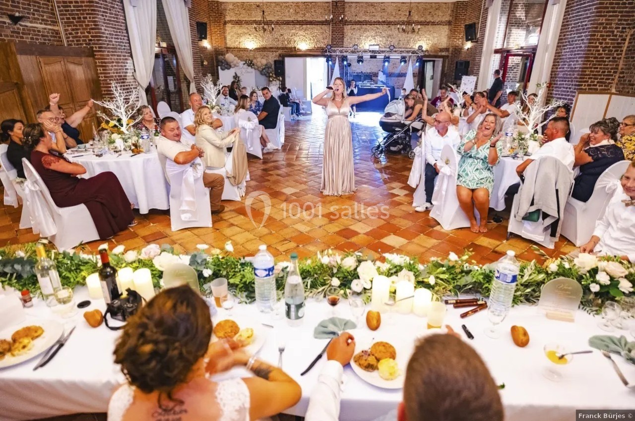 Une femme chante devant des invités assis à des tables décorées lors d'une réception dans une salle en briques.