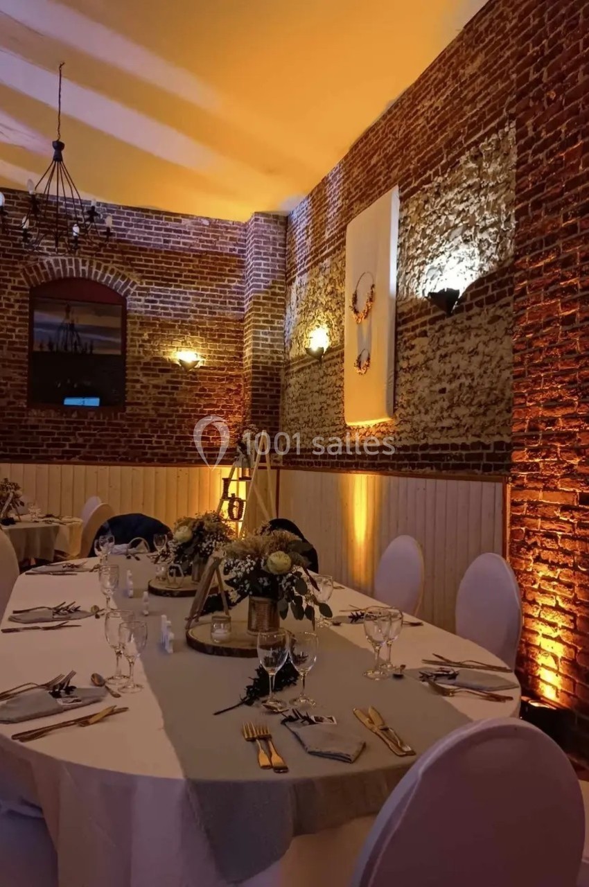 Salle de réception en briques avec éclairage chaleureux, grande table décorée de fleurs et vaisselle élégante.