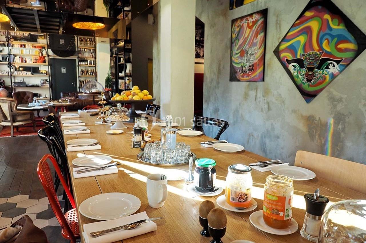 Grande table en bois dressée pour un repas, entourée de chaises, dans une pièce décorée avec des œuvres d'art et des…