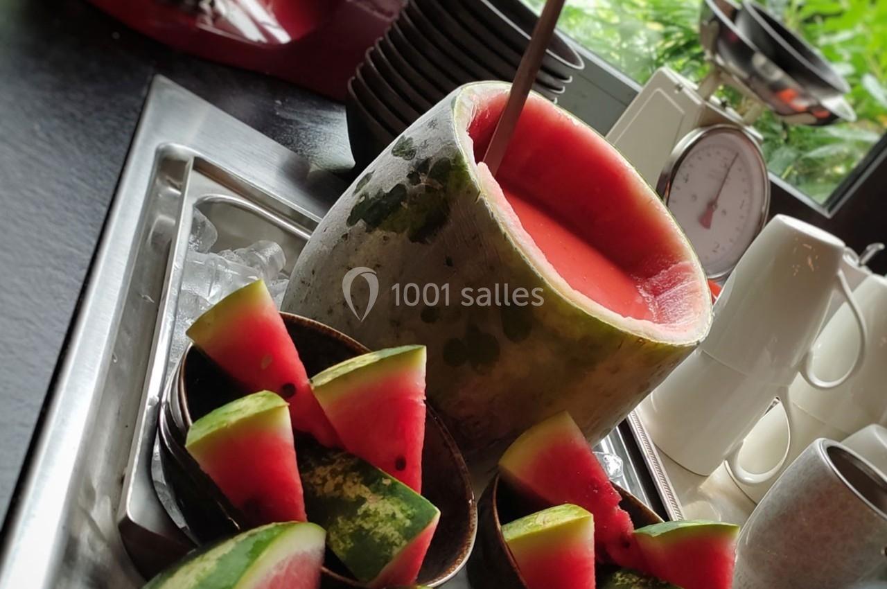 Pastèque évidée remplie de jus, entourée de tranches de pastèque sur un plan de travail près d'une fenêtre.