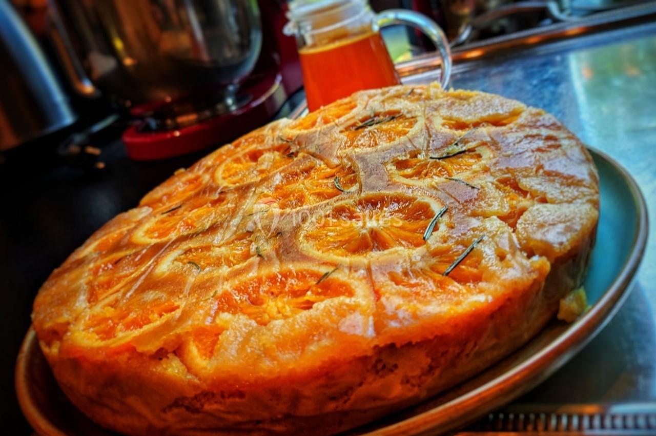 Gâteau renversé aux oranges caramélisées posé sur une assiette dans une cuisine avec un pot de miel en arrière-plan.
