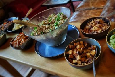 Salade de quinoa dans un grand bol entourée de petits plats contenant divers légumes sur une table en bois.