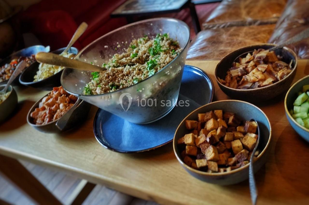 Salade de quinoa dans un grand bol entourée de petits plats contenant divers légumes sur une table en bois.