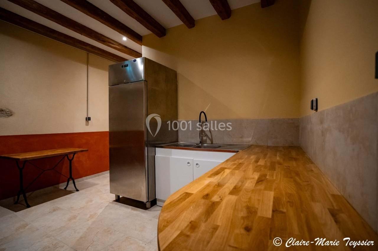 Cuisine minimaliste avec plan de travail en bois, évier inox, réfrigérateur et table pliante sur sol carrelé.