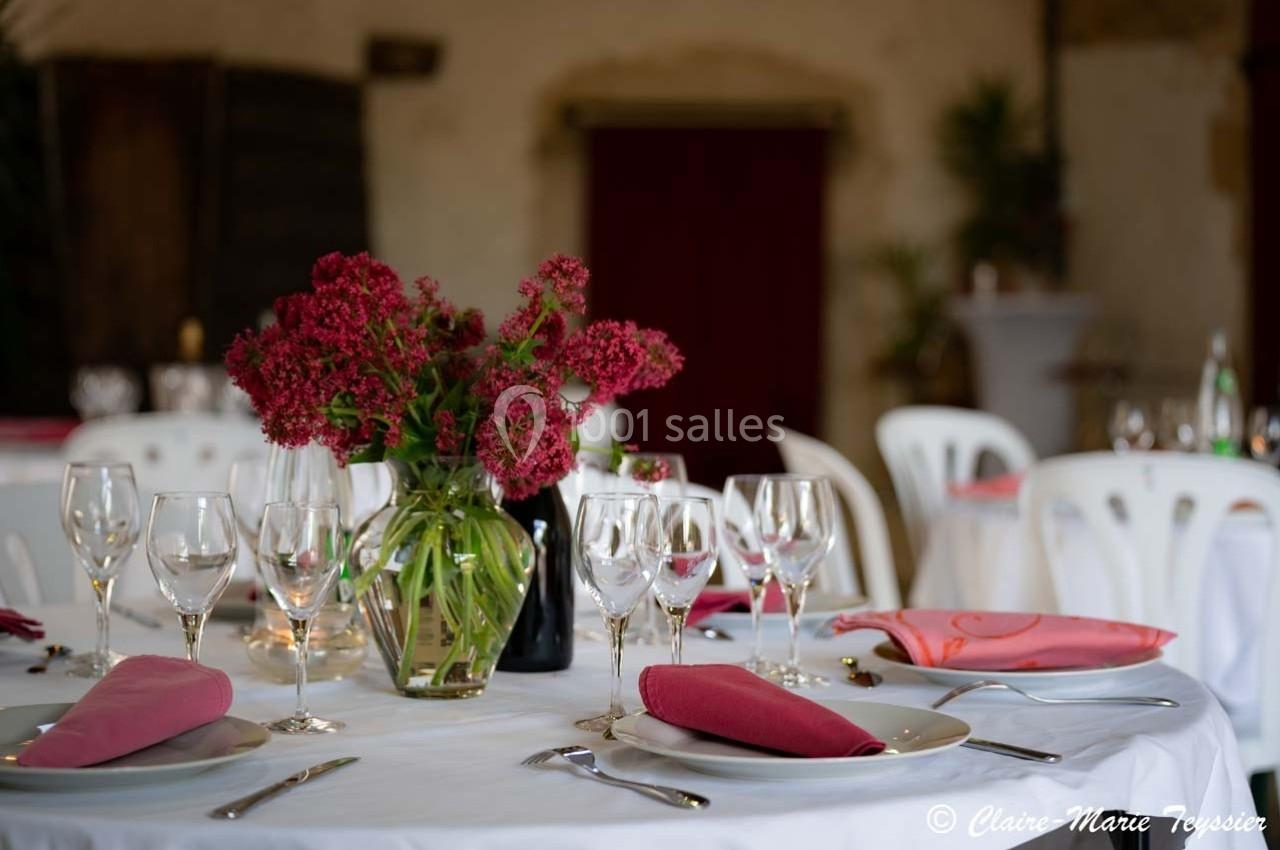 Table dressée avec des verres, assiettes et serviettes roses, décorée d'un bouquet de fleurs rouges dans un vase.