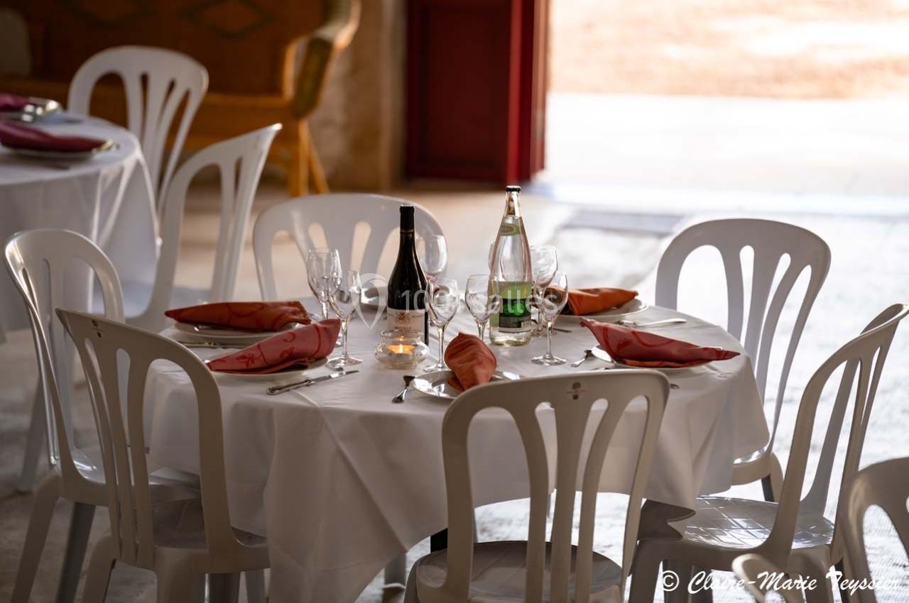 Table ronde dressée avec nappes blanches, chaises en plastique, verres, serviettes rouges, bouteille de vin et eau.