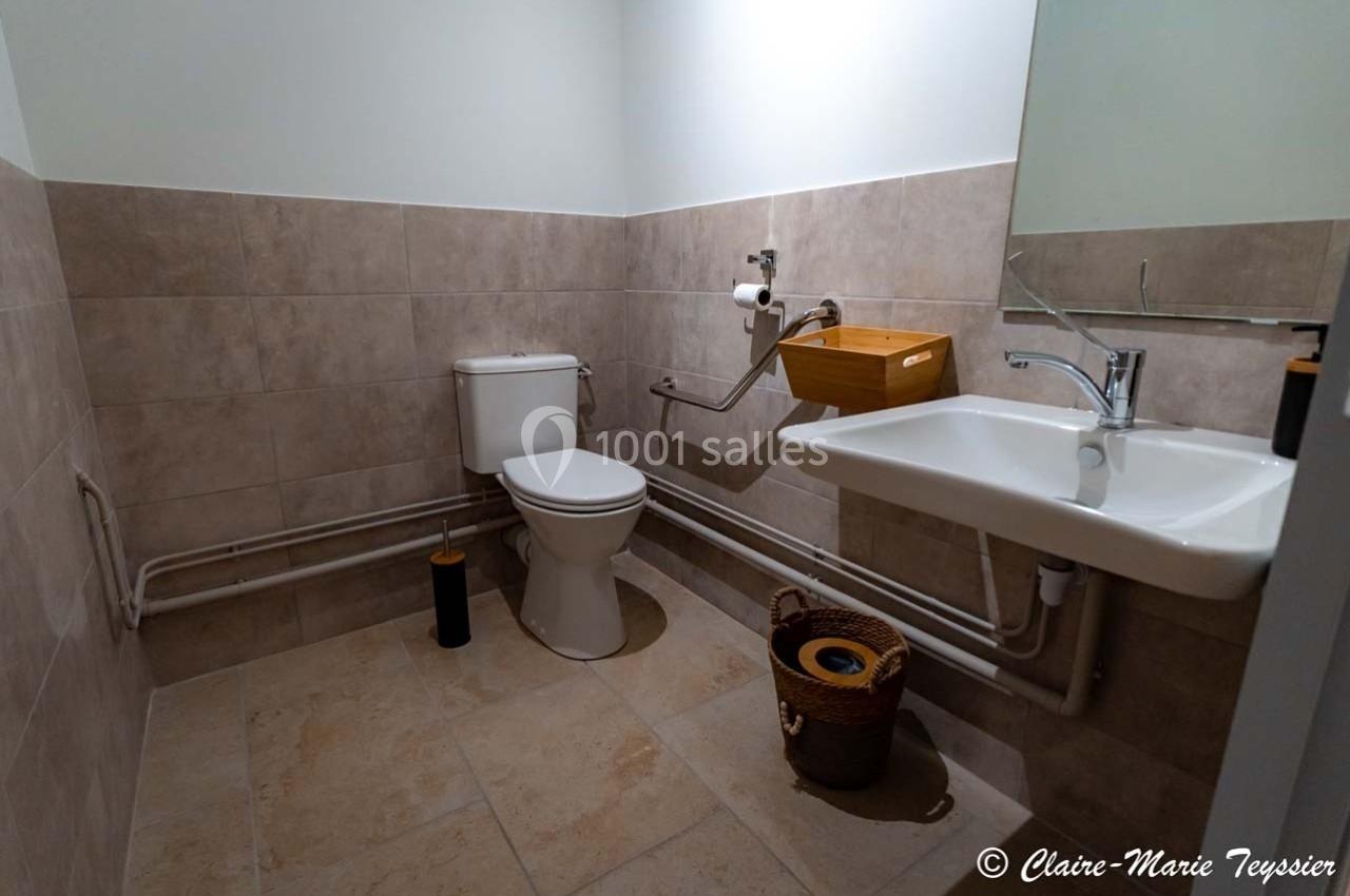 Toilettes accessibles avec lavabo, miroir, barre d'appui et carrelage beige au mur et au sol.