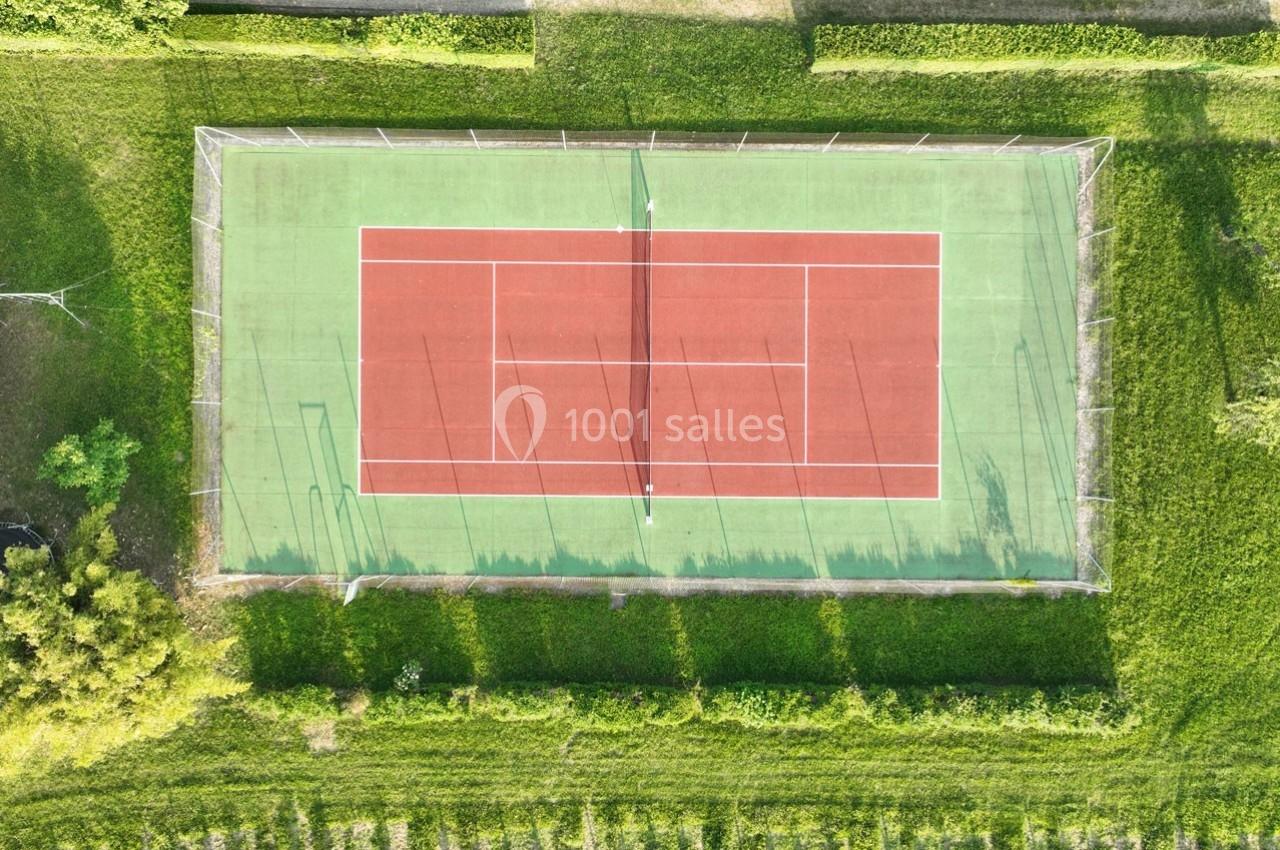 Vue aérienne d'un court de tennis en plein air entouré de pelouses et de haies.