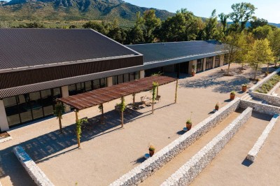Terrasse ombragée avec pergola en bois, tables et chaises devant un bâtiment moderne avec de grandes baies vitrées.