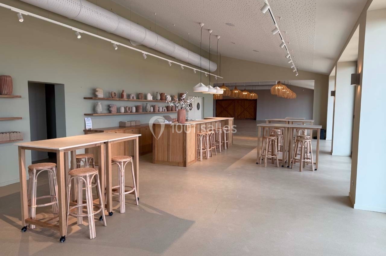 Salle lumineuse avec tables hautes en bois, tabourets et étagères décorées de vases dans un style épuré.