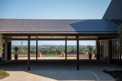 Terrasse ombragée avec pergola en bois, tables et chaises devant un bâtiment moderne avec de grandes baies vitrées.
