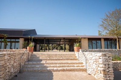 Terrasse ombragée avec pergola en bois, tables et chaises devant un bâtiment moderne avec de grandes baies vitrées.
