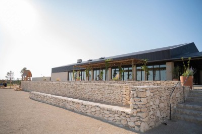 Terrasse ombragée avec pergola en bois, tables et chaises devant un bâtiment moderne avec de grandes baies vitrées.