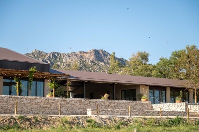 Terrasse ombragée avec pergola en bois, tables et chaises devant un bâtiment moderne avec de grandes baies vitrées.