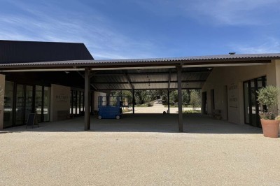 Terrasse ombragée avec pergola en bois, tables et chaises devant un bâtiment moderne avec de grandes baies vitrées.