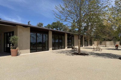 Terrasse ombragée avec pergola en bois, tables et chaises devant un bâtiment moderne avec de grandes baies vitrées.