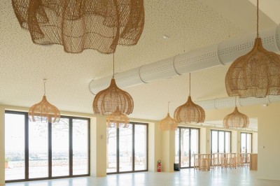 Terrasse ombragée avec pergola en bois, tables et chaises devant un bâtiment moderne avec de grandes baies vitrées.