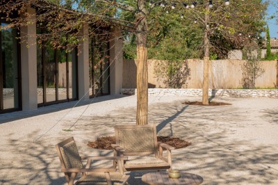 Terrasse ombragée avec pergola en bois, tables et chaises devant un bâtiment moderne avec de grandes baies vitrées.
