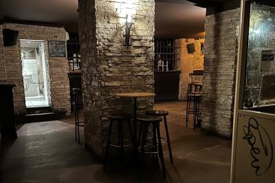 Intérieur d'un bar avec comptoir en bois, tabourets hauts, murs en pierre et éclairage tamisé.