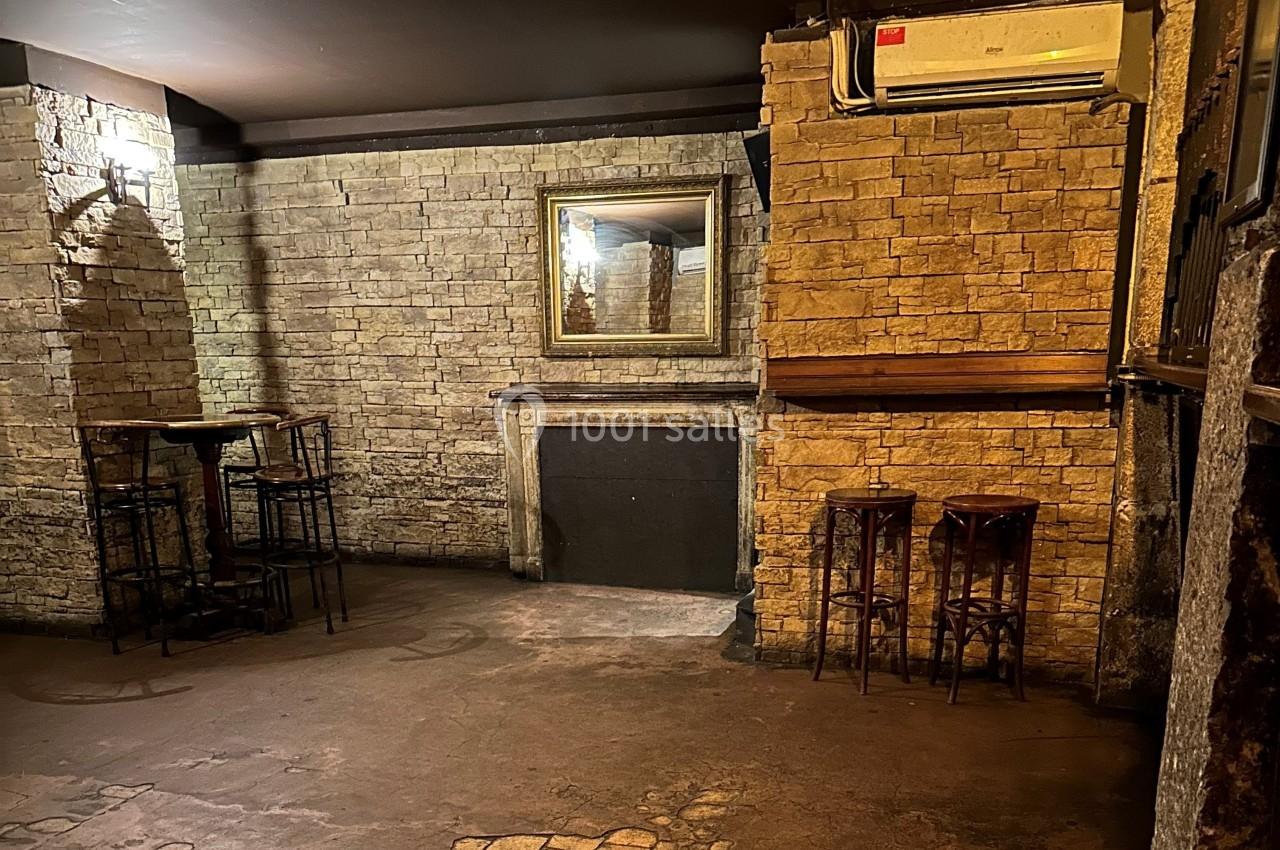 Salle avec murs en pierre, cheminée décorative, table haute avec tabourets et miroir encadré au mur.