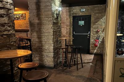 Intérieur d'un bar avec comptoir en bois, tabourets hauts, murs en pierre et éclairage tamisé.