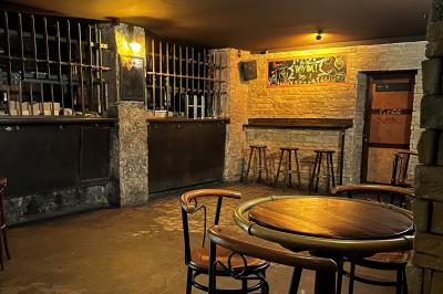 Intérieur d'un bar avec comptoir en bois, tabourets hauts, murs en pierre et éclairage tamisé.