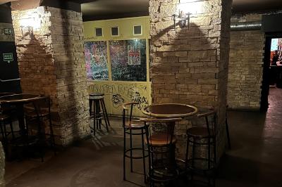 Intérieur d'un bar avec comptoir en bois, tabourets hauts, murs en pierre et éclairage tamisé.