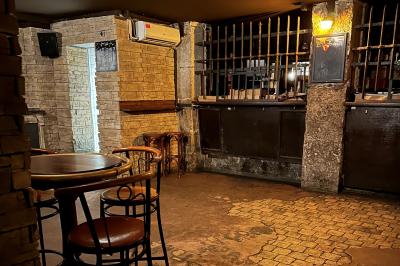 Intérieur d'un bar avec comptoir en bois, tabourets hauts, murs en pierre et éclairage tamisé.