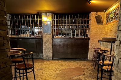 Intérieur d'un bar avec comptoir en bois, tabourets hauts, murs en pierre et éclairage tamisé.