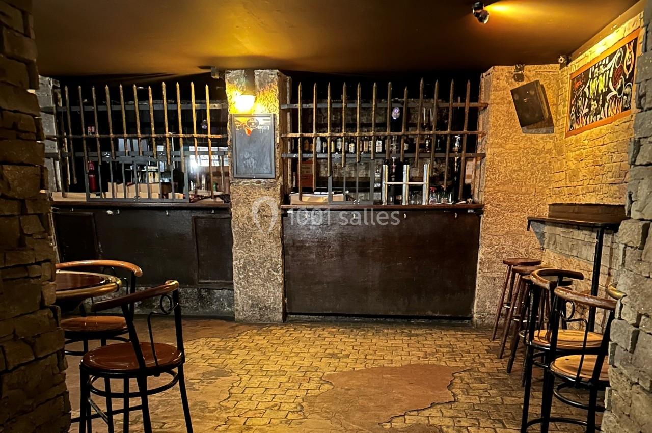 Intérieur d'un bar avec comptoir en bois, tabourets hauts, murs en pierre et éclairage tamisé.